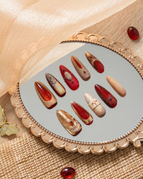 Luxury press on nails with ruby red, gold, and nude tones, inspired by ancient Egyptian art, displayed in an elegant decorative flat lay.