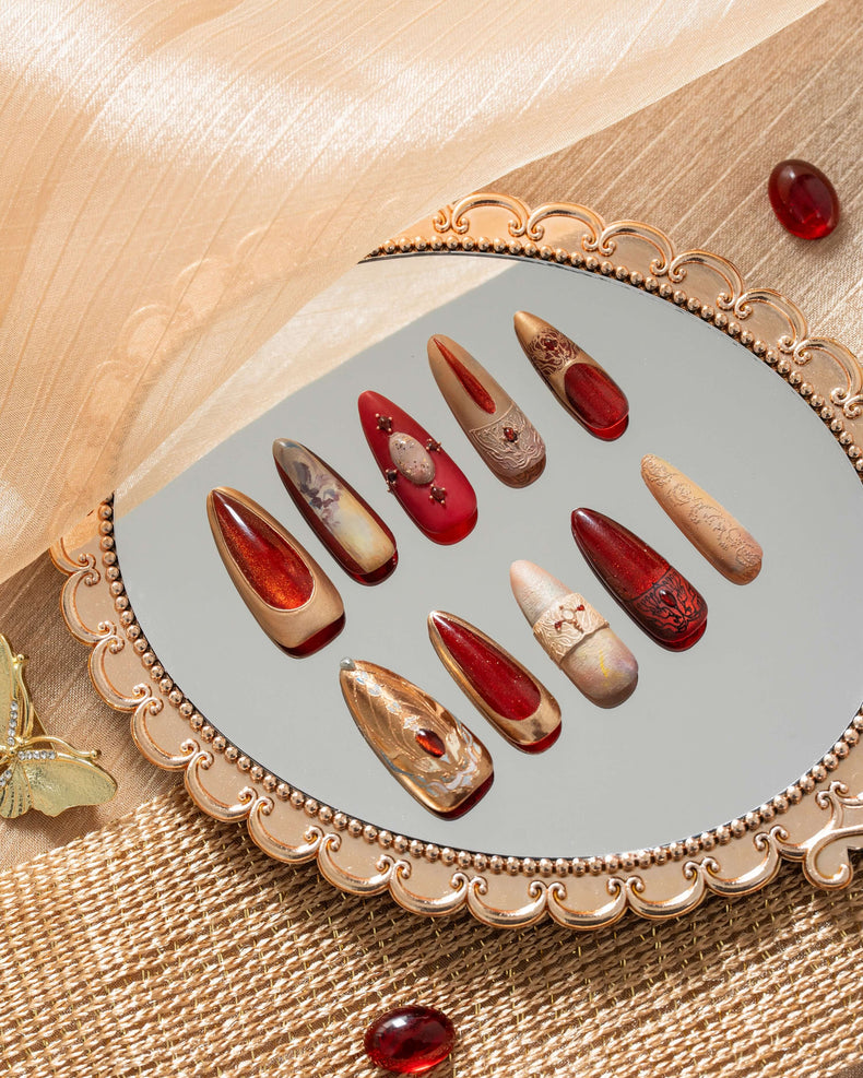 Luxury press on nails with ruby red, gold, and nude tones, inspired by ancient Egyptian art, displayed in an elegant decorative flat lay.