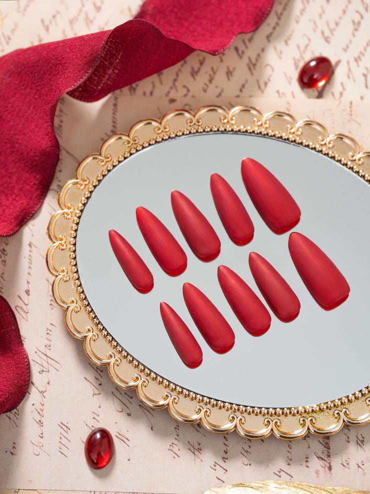 Matte velvet red press on nails in an elegant almond shape, displayed in a luxury flat lay with gold accents and a refined, timeless aesthetic.