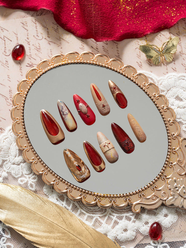 Luxury press on nails with ruby red, gold, and nude tones, inspired by ancient Egyptian art, displayed in an elegant decorative flat lay.