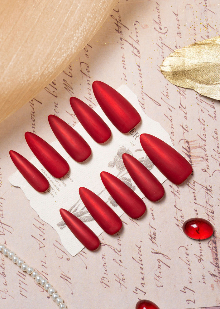 Matte velvet red press on nails in an elegant almond shape, displayed in a luxury flat lay with gold accents and a refined, timeless aesthetic.