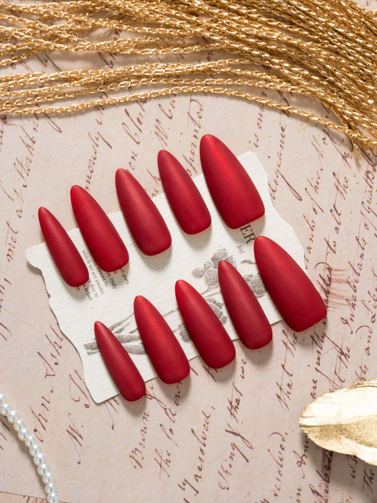 Matte velvet red press on nails in an elegant almond shape, displayed in a luxury flat lay with gold accents and a refined, timeless aesthetic.