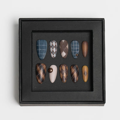 A set of ten press-on nails displayed inside a black square frame, featuring various patterns including plaid, argyle, and solid colors in shades of brown, blue, beige, and white, set against a plain light gray background.