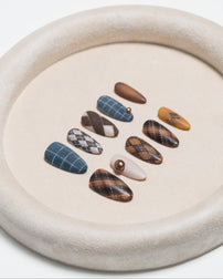 A set of ten press-on nails with various patterns including plaid, argyle, and solid colors, displayed on a beige textured circular tray.