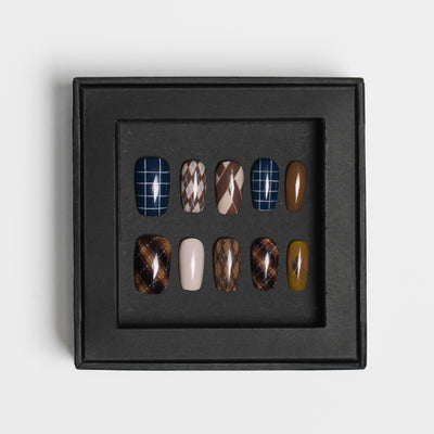 A set of ten press-on nails displayed in a black square tray against a light gray background. The nails feature various patterns including plaid, argyle, leopard print, solid brown, and solid beige.