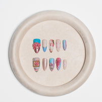 A set of decorative press-on nails displayed on a round beige stand against a clean white background.