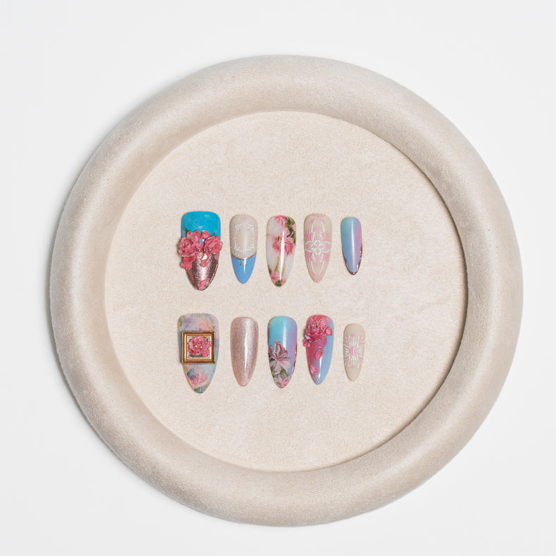 A set of decorative press-on nails displayed on a round beige stand against a clean white background.