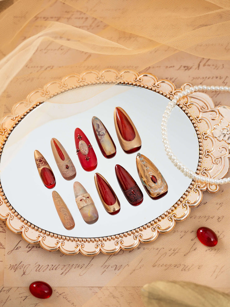 Luxury press on nails with ruby red, gold, and nude tones, inspired by ancient Egyptian art, displayed in an elegant decorative flat lay.