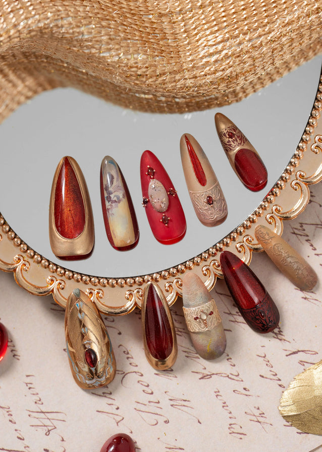 Luxury press on nails with ruby red, gold, and nude tones, inspired by ancient Egyptian art, displayed in an elegant decorative flat lay.